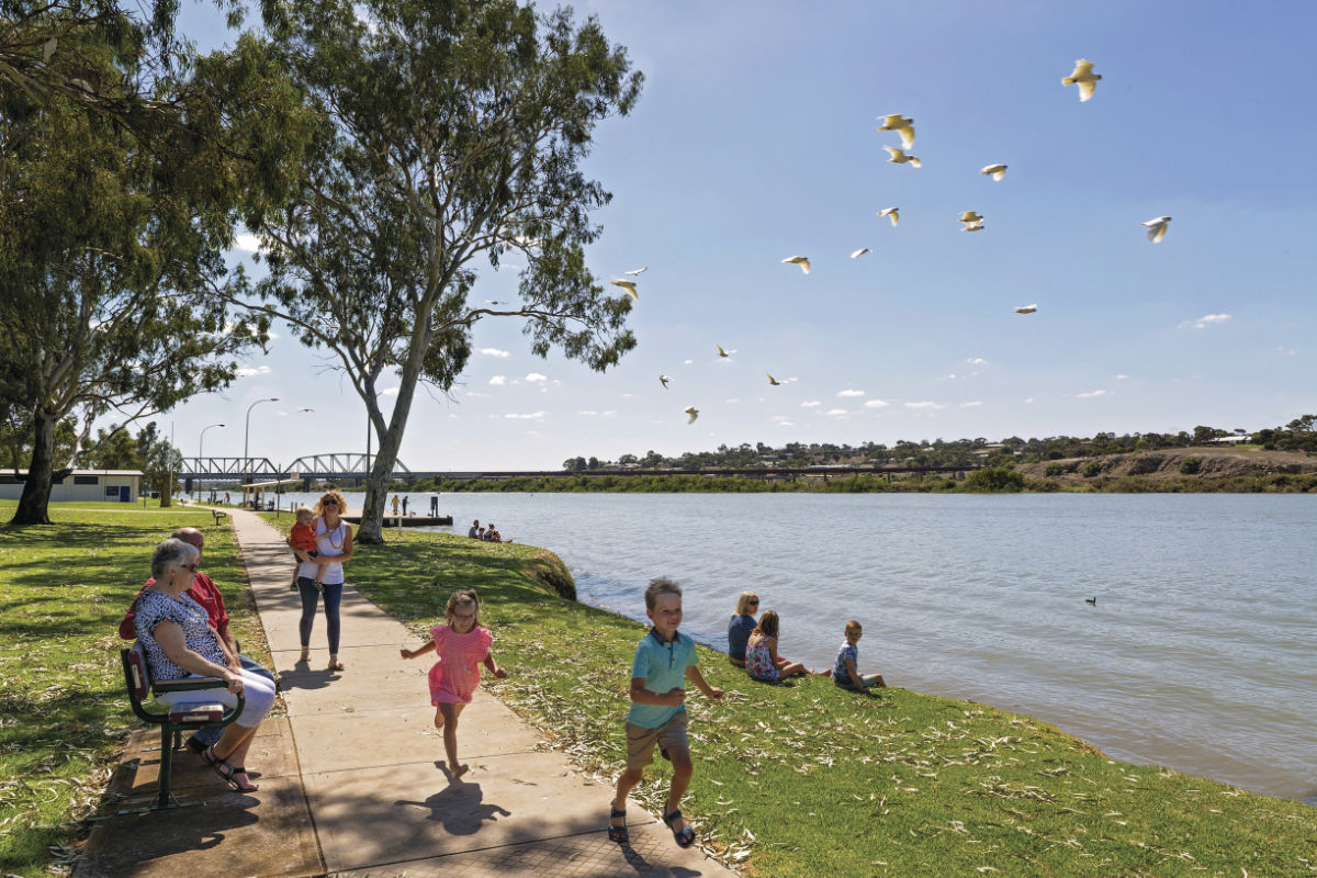 Couple sitting on park bench by river watching children playing